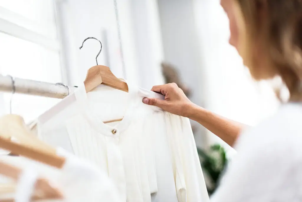 Hand prüft eine weiße Bluse auf einem Holzbügel